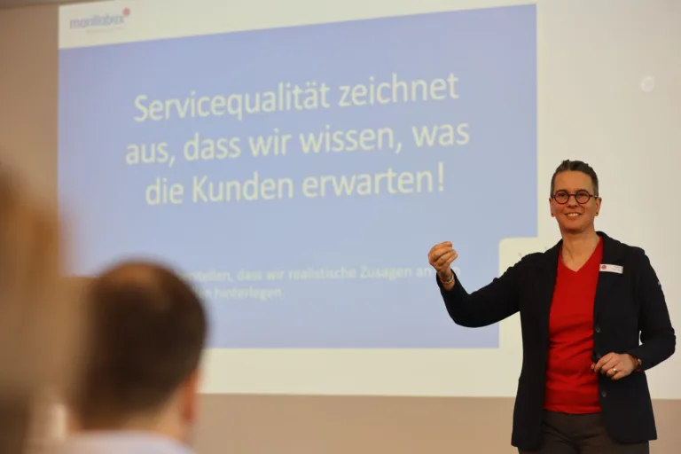 Marilla Bax vor der Folie „Servicequalität zeichnet aus, dass wir wissen, was die Kunden erwarten!“