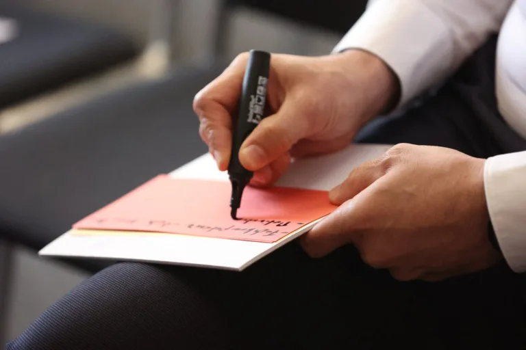 Hand beschriftet eine rote Moderationskarte mit dem Marker
