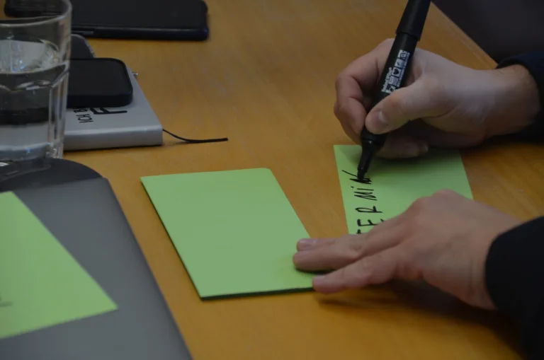Hand schreibt am Workshoptisch auf eine grüne Karte