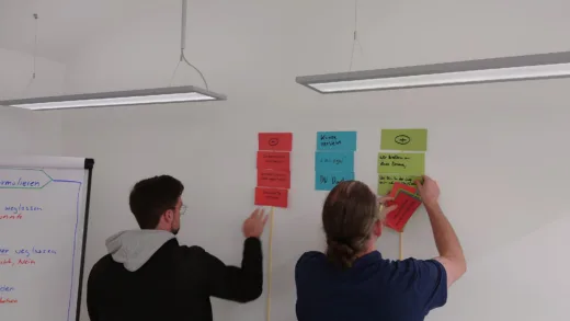 Zwei Teilnehmende kleben Moderationskarten an eine Wand